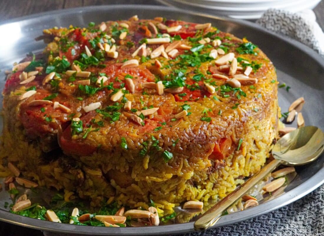 The ingredients are layered in a pot: vegetables at the bottom, followed by meat, and then rice. The pot is simmered until cooked, then inverted onto a large tray or dish before serving.