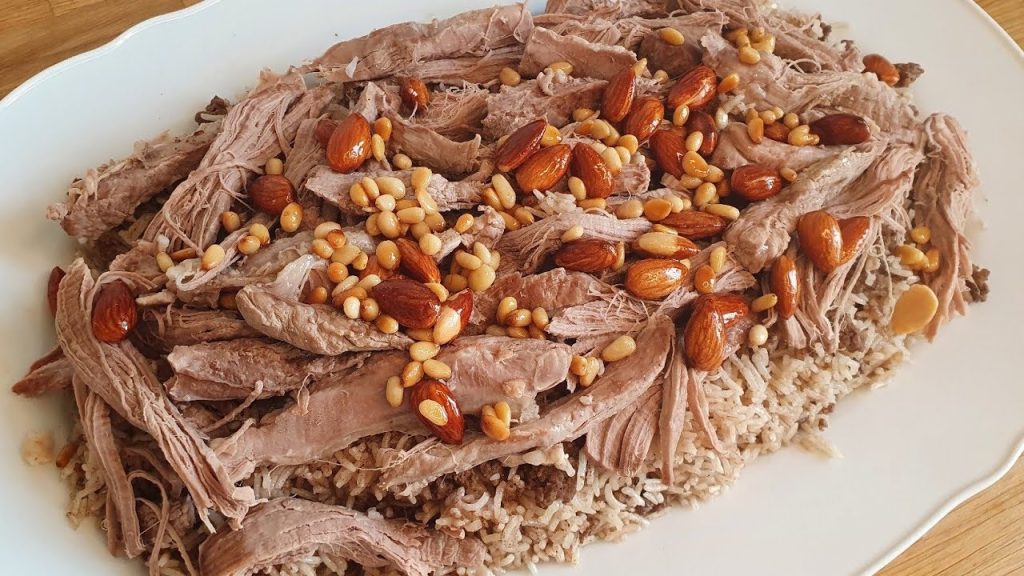 Lamb ribs are seasoned and slow-cooked with spices, while rice is prepared with minced meat, saffron, and olive oil. The ribs are served over the rice and often paired with yogurt or laban.