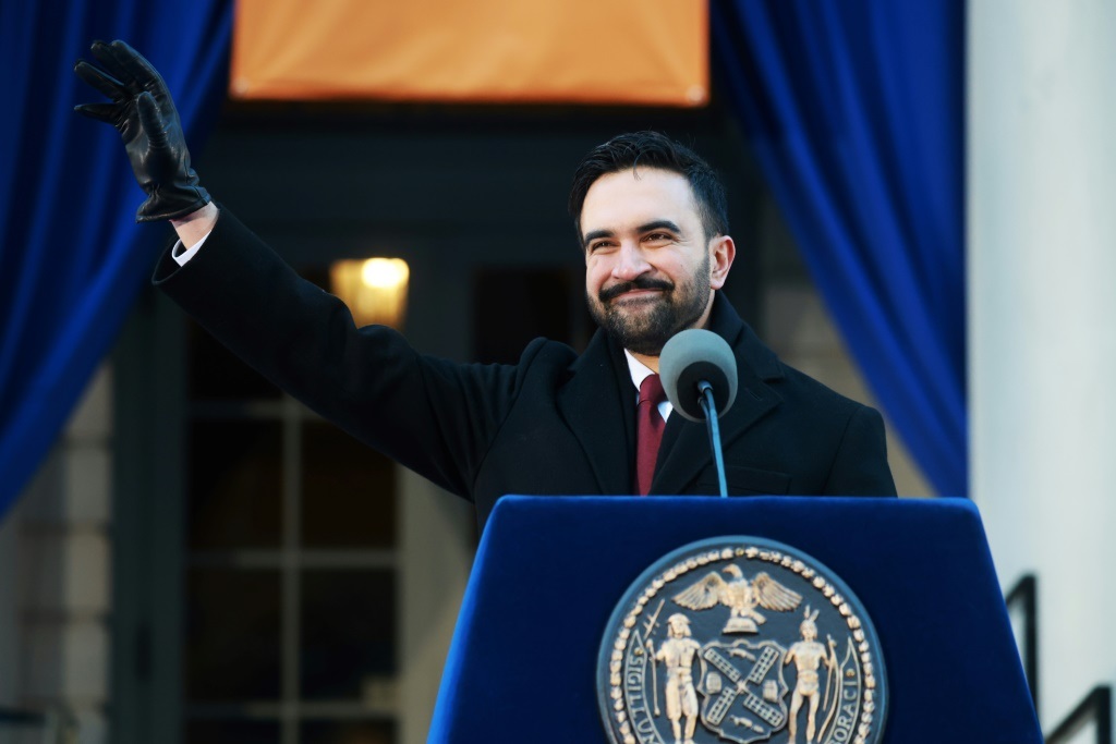 Dressed in heavy clothing to withstand the bitter cold and visibly battling a cold, Mamdani was accompanied by a camera crew. He repeatedly stopped to greet neighbors who wished him well. Aboard the Manhattan-bound train, under limited security, the new mayor agreed to take selfies with surprised commuters before settling into a corner seat to review briefing materials for his first day. When two French tourists doubted his identity, Mamdani introduced himself as “the new mayor of New York City” and showed them a copy of the New York Daily News featuring his photo on the front page. While riding the subway is not unprecedented for New York City mayors—Eric Adams, Bill de Blasio, and Michael Bloomberg all did so—images of Mamdani spread rapidly on social media. Supporters viewed them as a visual fulfillment of his inaugural pledge that his administration would “look like and live like the people it represents.”